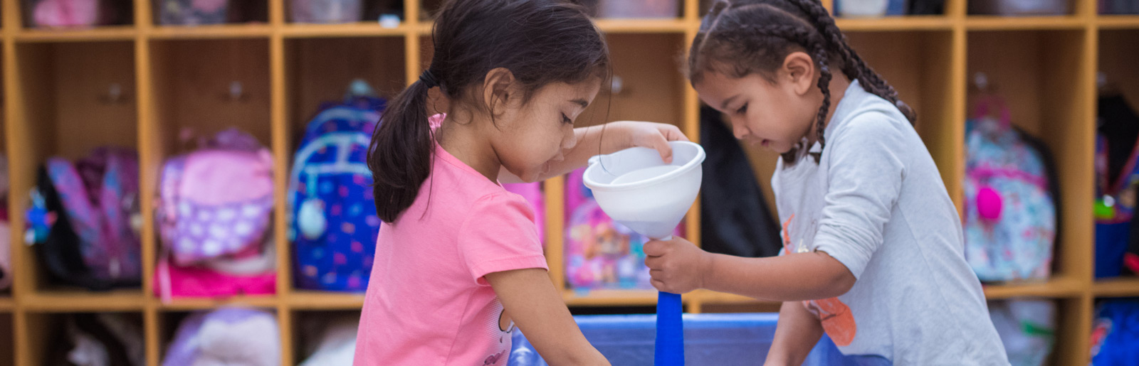 two girls use a plastic funnel in an activity