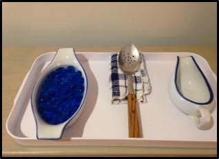 bowl, spoon, and bowl on a platter with blue marbles in the left bowl