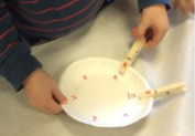 child putting clothes pins on paper plate
