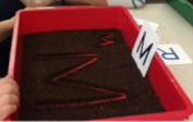 the letter M drawn in dirt