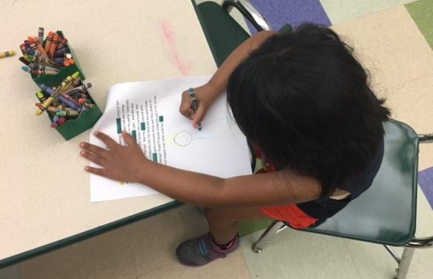child drawing a picture under the typed dictation of their story