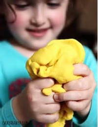 Girl squishing yellow playdough with a smile on her face looking satisfied.