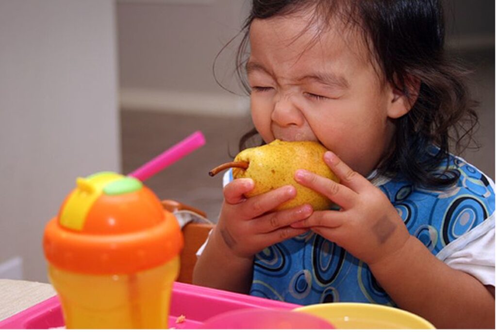 A young girl biting a pear.