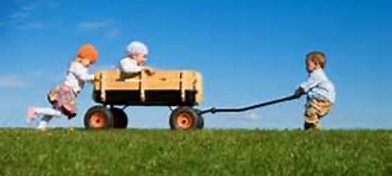 A young boy pulling a wooden wagon with a child in it while another child is pushing the wagon.