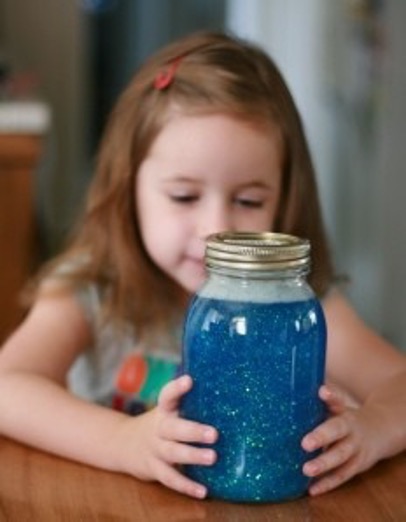 A girl looking at a jar filled with blue liquid containing sparkles.
