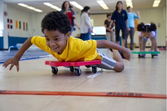 A boy laying on a flat scooter pushing himself with his arms.