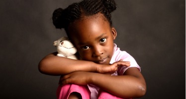 A girl holding a stuffed animal looking at the camera.