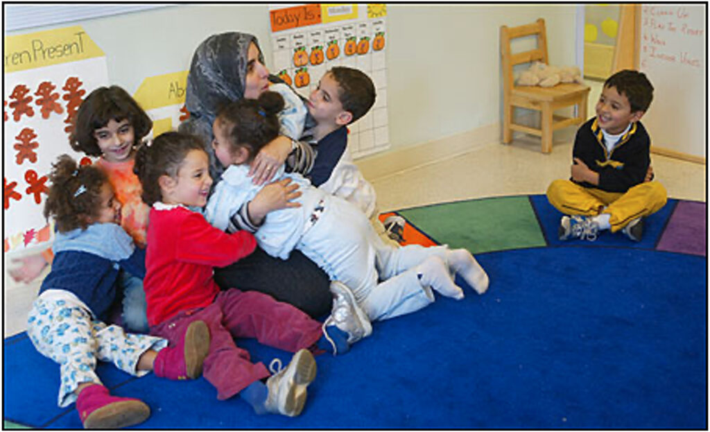 Preschool children hugging their teacher and each other on the rug.