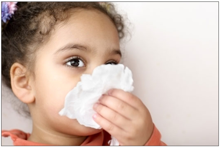 A girl blowing her nose with a tissue.