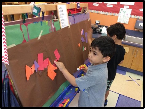 Child attaching torn paper to contact paper at the easel