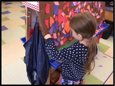 Child attaching torn paper to contact paper at the easel