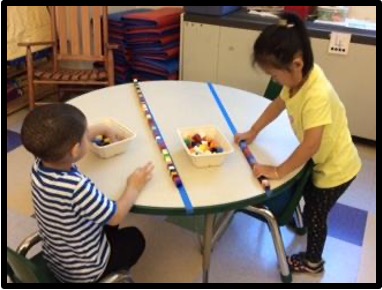 Two children connecting Unifix cubes across a masking tape line