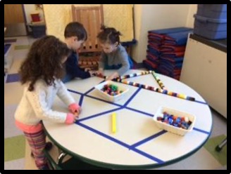 Three children connecting Unifix cubes across lines of tape on a circular table