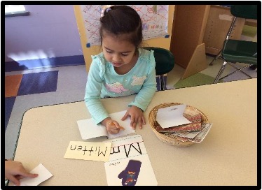 Child copying the word "Mitten" into a journal