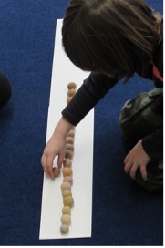 Child comparing and seriating up classroom-made skin-tone play dough balls from light to dark. 