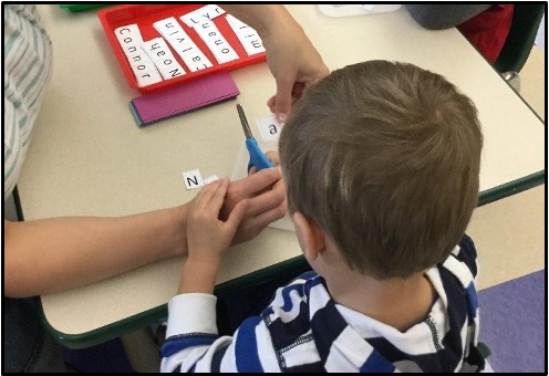 Child receiving hand over hand scissor guidance from teacher