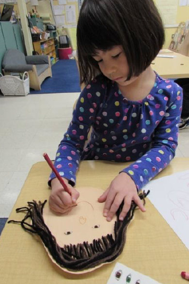 girl making a face on construction paper and yarn